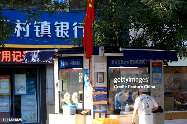 Medical worker works in a Covid testing kiosk beside an outlet of a rural bank in Zhengzhou city in central China's Henan province Friday, June 17,...