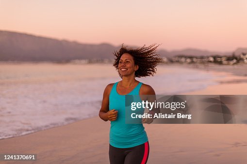 Female jogger out for a run along beach at sunset Female jogger out for a run along beach at sunset
