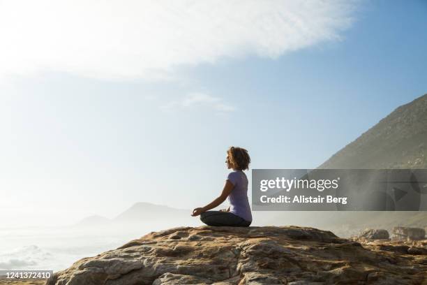 woman meditating on rock by the sea - meditation outdoors fotografías e imágenes de stock