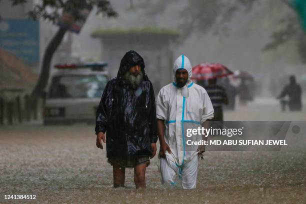 People wade along a road in a flooded area during a monsoon rainfall in Sylhet on June 18, 2022. Monsoon storms in Bangladesh and India have killed...