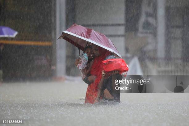 Woman with children wades along flooded street during a monsoon rainfall in Sylhet on June 18, 2022. Monsoon storms in Bangladesh and India have...