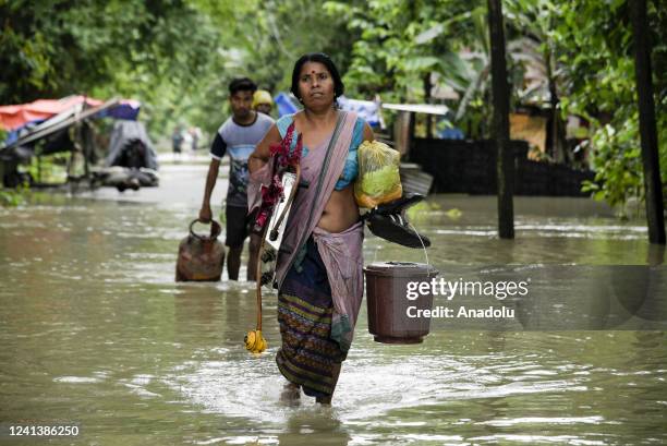 Flood affected people carries LPG cylinder and stove, wade through flood water after heavy rainfall, at a village on June 18, 2022 in Nalbari, India....