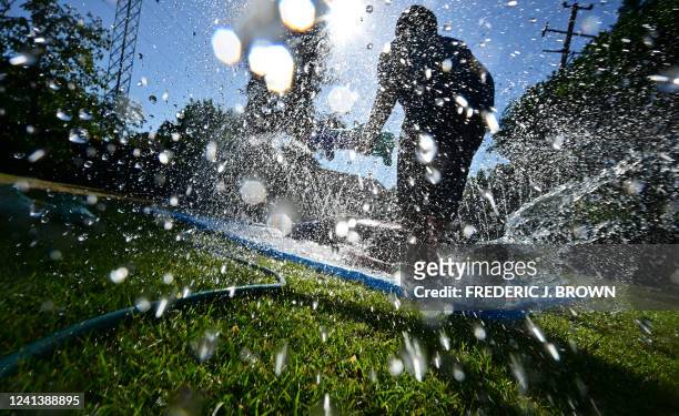 Water splashes as children cool off on a lawn sprinkler toy in Fresno, California, on June 17, 2022. Millions of Americans have been under some sort...