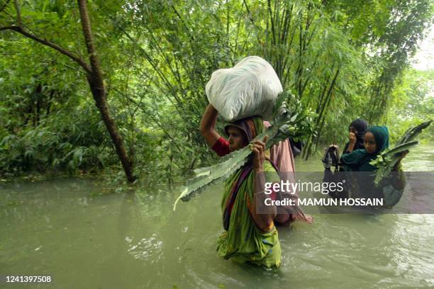 People wade along a road in a flooded area following heavy monsoon rainfalls in Companiganj on June 19, 2022.