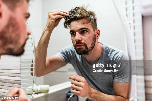 junger mann stilisiert seine haare im badezimmer - haare mann stock-fotos und bilder