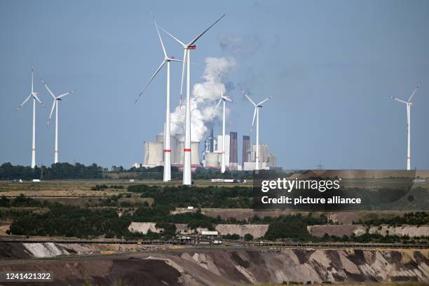 June 2022, North Rhine-Westphalia, Jüchen: Steam comes out of the cooling towers of the Neurath lignite-fired power plant, with wind turbines in...