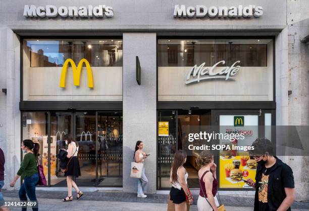 Pedestrians walk past the American multinational fast-food hamburger restaurant chain, McDonald's and McCafe logos in Spain.