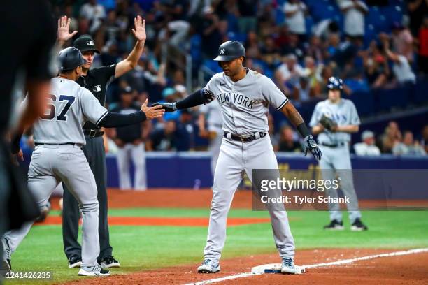 Aaron Hicks high fives third base coach Luis Rojas of the New York Yankees after hitting a triple off Jason Adam of the Tampa Bay Rays in the ninth...