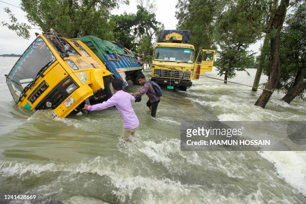 People wade past stranded trucks on a flooded street in Sunamganj on June 21, 2022. Floods are a regular menace to millions of people in low-lying...