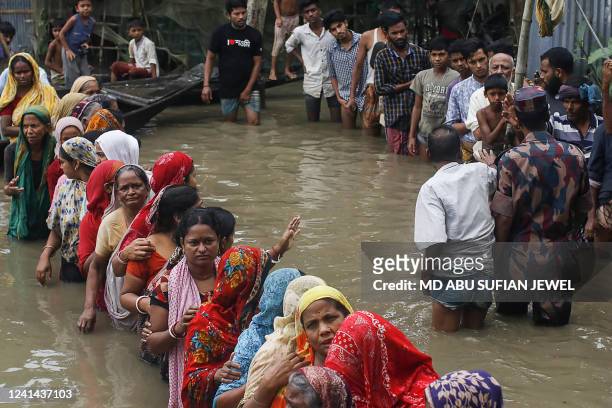 Flood affected people queue in knee-deep flood waters to collect food relief following heavy monsoon rainfalls in Sunamganj on June 21, 2022. At...