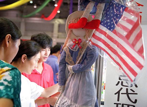 Shoppers check out the various toys on display beside a doll with a plastic American flag at a store in Beijing 07 July 2000. Chinese and US...
