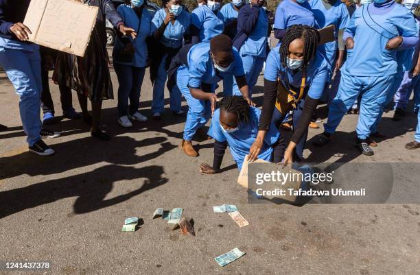 Nurses protest whilst holding placards in-front of the local currency which they are protesting against demanding their salaries in USD at...