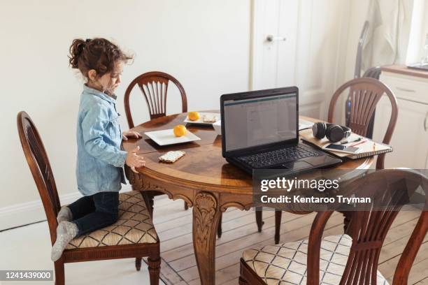 side view of girl looking at fruit in plate while kneeling on chair by table - agenouillé photos et images de collection