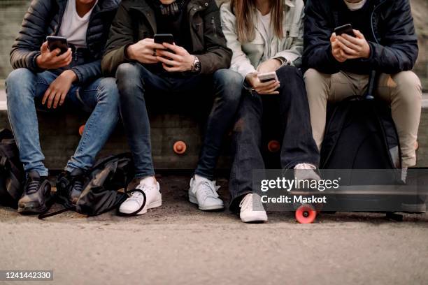 low section of teenage boys and girl using smart phone while sitting at park - jeunes garçons photos et images de collection