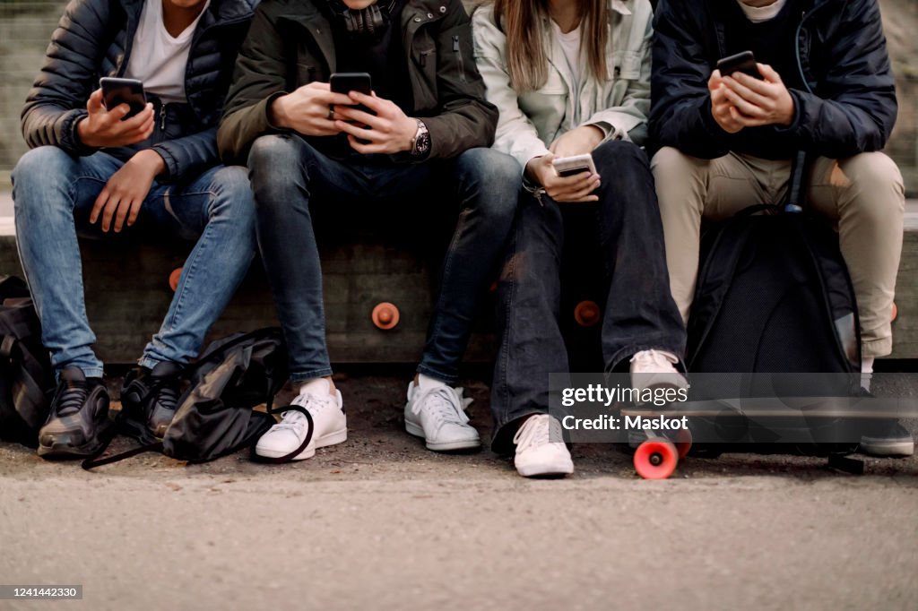 Low section of teenage boys and girl using smart phone while sitting at park