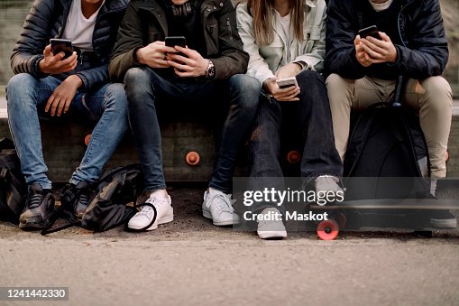 Low section of teenage boys and girl using smart phone while sitting at park Low section of teenage boys and girl using smart phone while sitting at park
