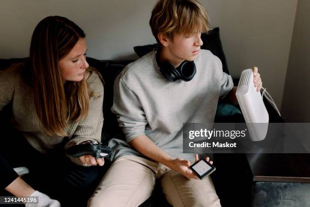 teenage boy checking wi-fi router while sitting with friend on sofa at home - internet router stock pictures, royalty-free photos & images