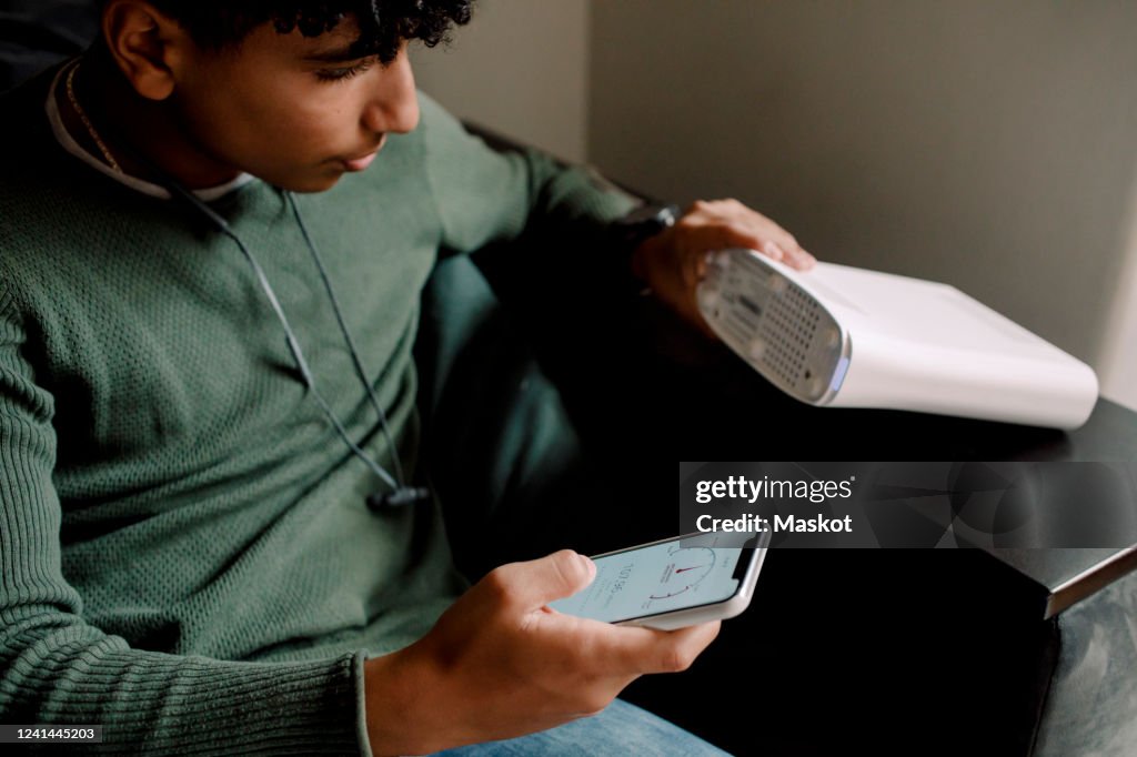 Teenage boy holding router while checking Wi-Fi connection on mobile phone at home