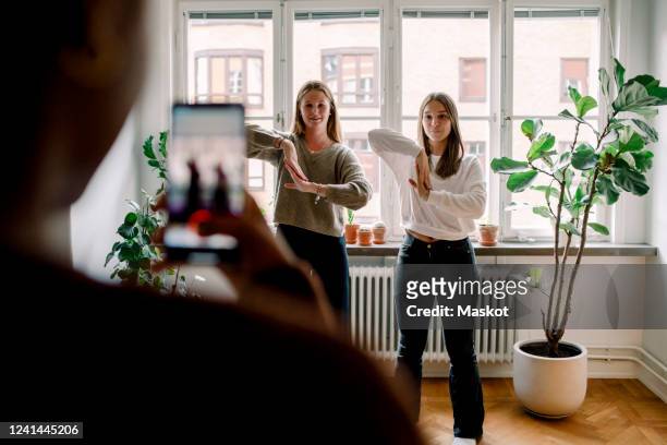 teenage girl with mobile phone filming female friends dancing against in living room - tipo di danza foto e immagini stock