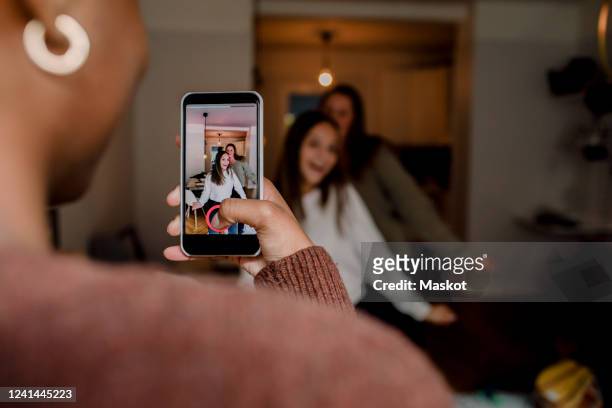 girl with smart phone filming teenage friends dancing in living room at home - digital native stock-fotos und bilder