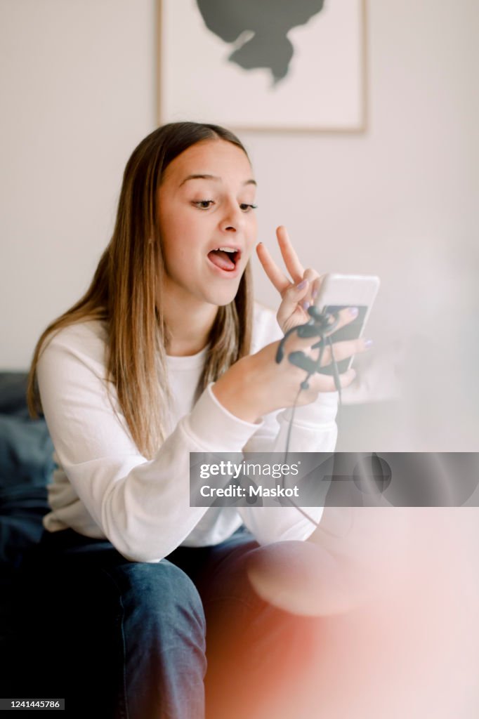 Teenage girl taking selfie through mobile phone while sitting at home