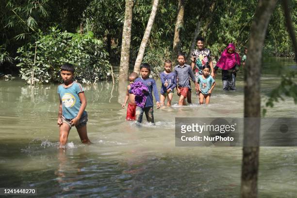People including children wade through flood water to receive food aid from Bangladesh Army in a flooded residential area following heavy monsoon...