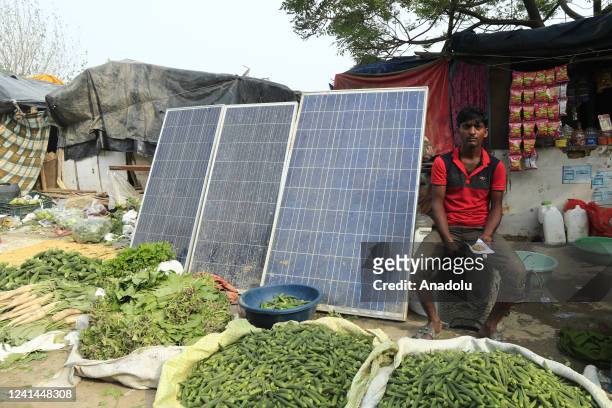 Indian shopkeeper sits near the solar panel placed outside a temporary settlement along the Yamuna river in New Delhi on the World Sustainable Energy...