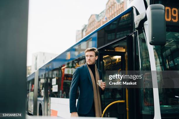 businessman with wrap sandwich looking away while standing against bus in city - bus wrap stockfoto's en -beelden