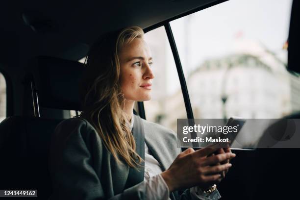 contemplating female entrepreneur with smart phone looking through window while sitting in taxi - taxi van stockfoto's en -beelden