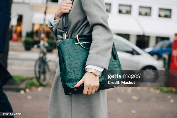 midsection of businesswoman with handbag standing in city - handtasche stock-fotos und bilder