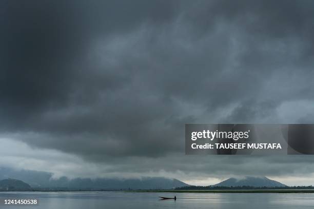 Boatman steers his boat as rain clouds loom over Dal Lake in Srinagar on June 22, 2022.