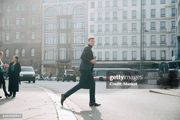 side view of entrepreneur walking on road against building in city - businessman city imagens e fotografias de stock
