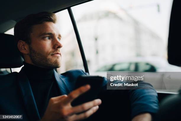 male entrepreneur with phone looking through window while sitting in taxi - car front view foto e immagini stock