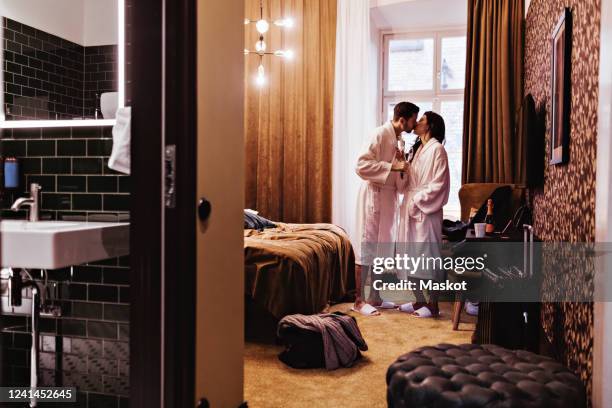 couple kissing while holding champagne flutes by bed in hotel room - couple and kiss and bedroom - fotografias e filmes do acervo