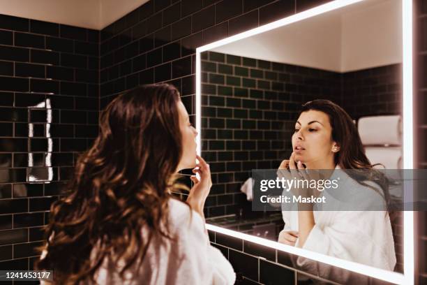 mid adult woman looking in mirror while applying lip balm - human lips stock pictures, royalty-free photos & images