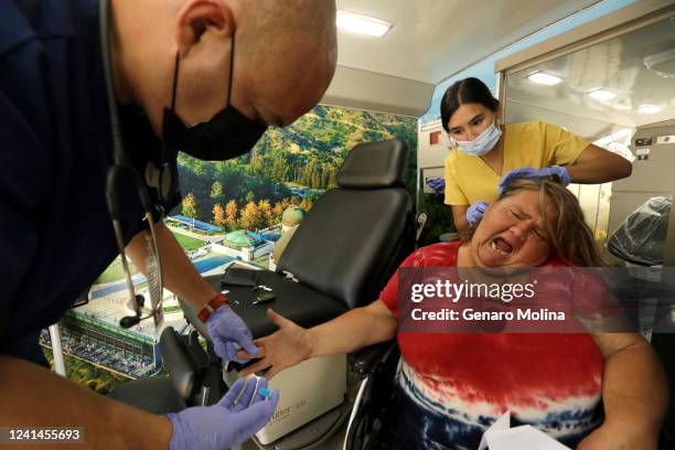Homeless patient Lisa Rogers grimaces after a prick by Saban Community Clinic medical assistant Jeffrey Figueroa, left, who checks her blood sugar...
