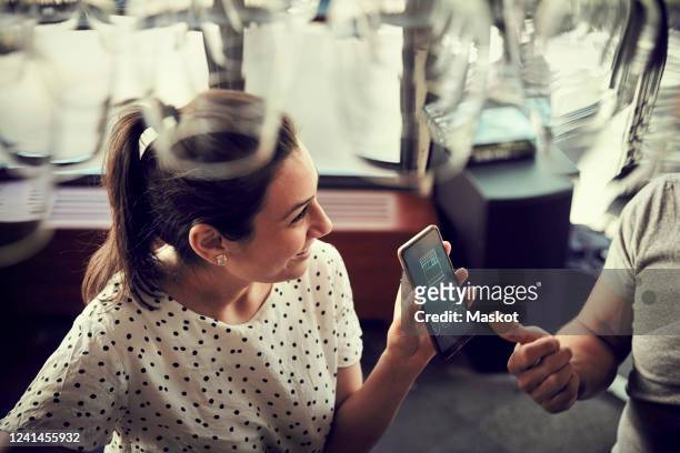 high angle view of smiling female showing smart phone to male partner in cafe - mobile screen stock-fotos und bilder