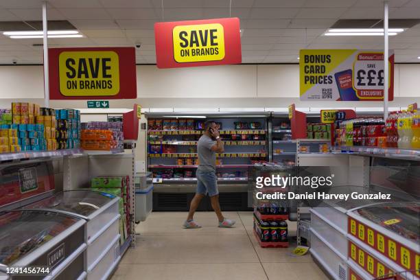 Man walks under a large sign hanging from the ceiling in the aisle of an Iceland supermarket advertises savings on popular food brands as the Office...