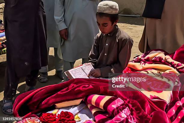 Graphic content / An Afghan boy reads from a religious book next to the body of an earthquake victim wrapped in a blanket before the burial rituals,...