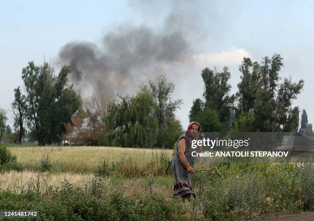 Woman speaks on a mobile phone on a roadside while smoke rises behind in the village Sviato-Pokrovske, Donetsk region, on June 23 amid Russia's...