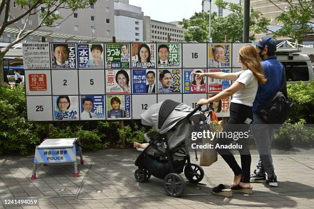 Couple and their baby watch portrait of candidates for the House of Councillors election set for July 10, displayed on the street on June 24, 2022 in...