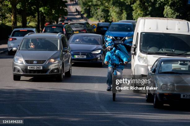 Cyclist looks over his shoulder to make eye contact with a motorist in an overtaking car on Sydenham Hill in south London, on 22nd June 2022, in...