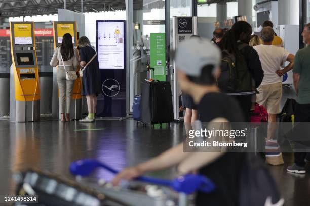 Travelers use a self-service check-in kiosk while other passengers queue at a customer service center for Deutsche Lufthansa AG at Terminal 1 of...
