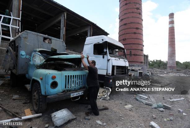 Worker of a farm of the 62-year-old owner Lyubov Zlobina examines destroyed car in the village of Mala Rohan, near Kharkiv, on June 23 amid Russian...