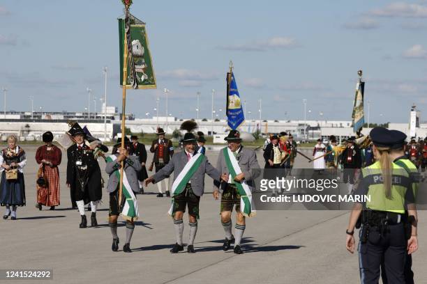 People dressed in traditional Bavarian clothes arrive to welcome France's President Emmanuel Macron upon his arrival at the Franz Josef Strauss...