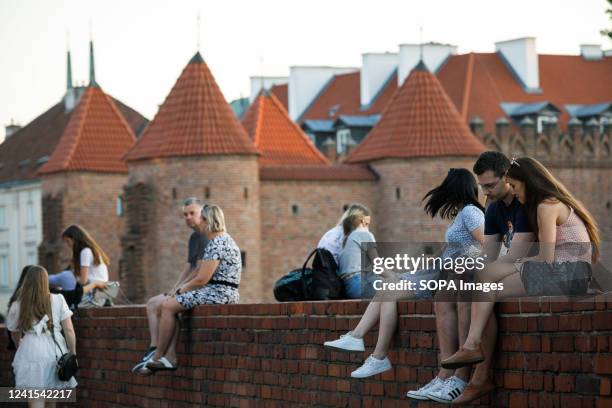 People enjoy the summer evening in Warsaw's Old Town while sitting at the old brick walls near the Warsaw Barbican. Daily life summer evening in...