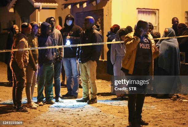 Members of the community and family wait for news outside a township pub as a police officer talks on a phone in South Africa's southern city of East...