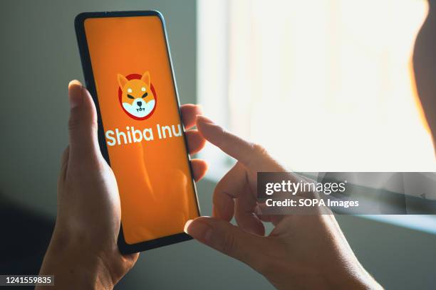 In this photo illustration, a woman holds a smartphone with the Shiba Inu logo displayed on the screen.