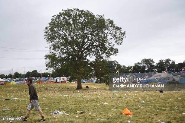 Festivalgoer walks past tents and garbage littering the venue at the end of the Glastonbury festival near the village of Pilton in Somerset,...