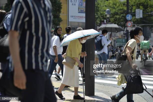 An old person walks on the street using an umbrella to protect herself from the sun on June 27 in Tokyo's popular Shibuya district in Tokyo, Japan....